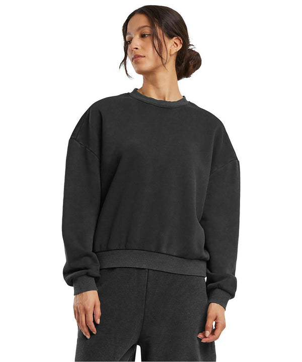 A woman wears the Build Your Brand Women's vintage heavy crew neck in black, paired with matching black joggers, standing against a plain white background.