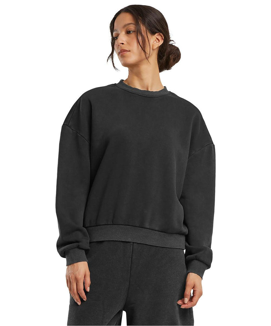 A woman wears the Build Your Brand Women's vintage heavy crew neck in black, paired with matching black joggers, standing against a plain white background.