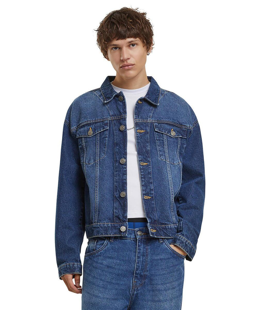A person with short brown hair wears the Build Your Brand Heavy Ounce Boxy Denim Jacket over a white T-shirt and blue jeans, standing against a plain white background with one hand in their pocket.