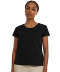 A person stands facing forwards against a plain white background, wearing the Build Your Brand Women's Sorona regular tee in black with light-coloured trousers.