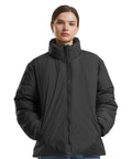 A person wears the Build Your Brand Women's loose puffer jacket in black, featuring a high collar and zip, hands in pockets, against a plain white background.