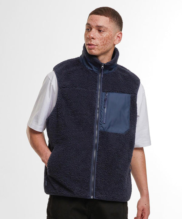 A person wearing the Build Your Brand Bonded Sherpa Gilet in navy blue with a contrasting chest pocket over a white short-sleeve t-shirt, standing with one hand in their pocket against a plain background.