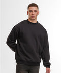 A person with short hair and freckles stands against a plain white background, wearing a Build Your Brand loose-fit sweatshirt in black and dark trousers, with one hand behind their back.
