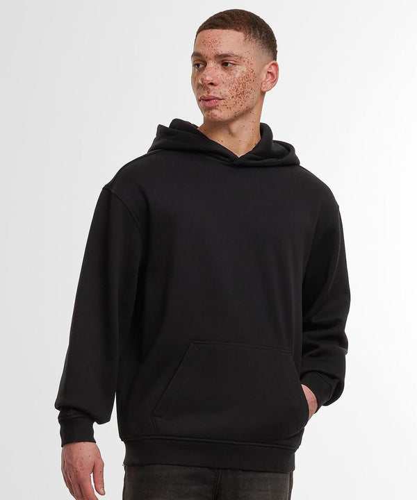 A person models the Build Your Brand loose-fit hoodie in black with dark jeans, standing against a white background and gazing to the side, one hand in the hoodie pocket.