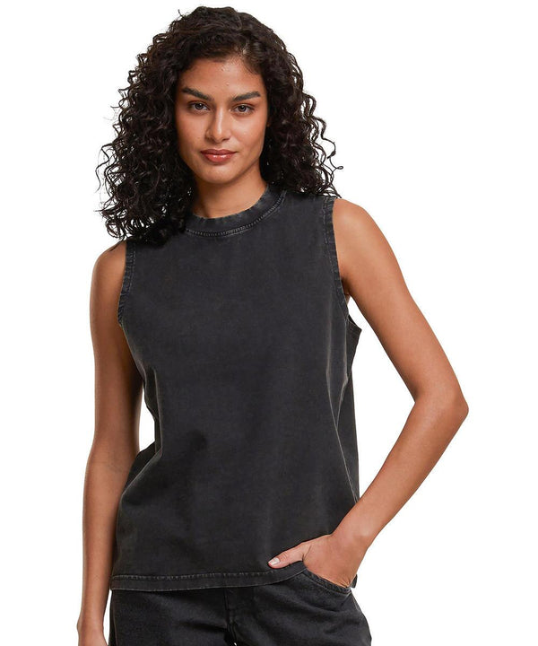 A person with curly hair wears the Build Your Brand Women's vintage washed sleeveless tee in faded black and matching black trousers, posing with one hand in their pocket against a plain white background.