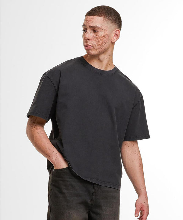 A person with short hair and freckles wears the Build Your Brand Vintage Cropped Heavy Oversized Tee in faded black, paired with black jeans, standing with one hand in their pocket and looking to the side against a plain background.