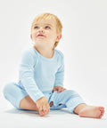 A baby with light hair, wearing a Babybugz BZ013 light blue onesie, is sitting on the floor against a plain white background, looking upward.