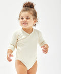 A smiling toddler in a light-colored long-sleeve BZ060 onesie by Babybugz stands against a plain white background.
