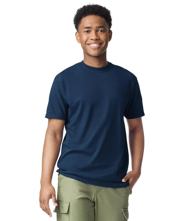 A young man smiles at the camera, wearing a Comfort Colours Heavyweight adult t-shirt in navy blue with olive green cargo trousers, set against a white background.