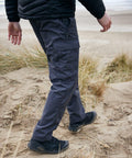 A person wearing Craghoppers CR231 cargo pants and black shoes walks through a sandy landscape with dry grasses.