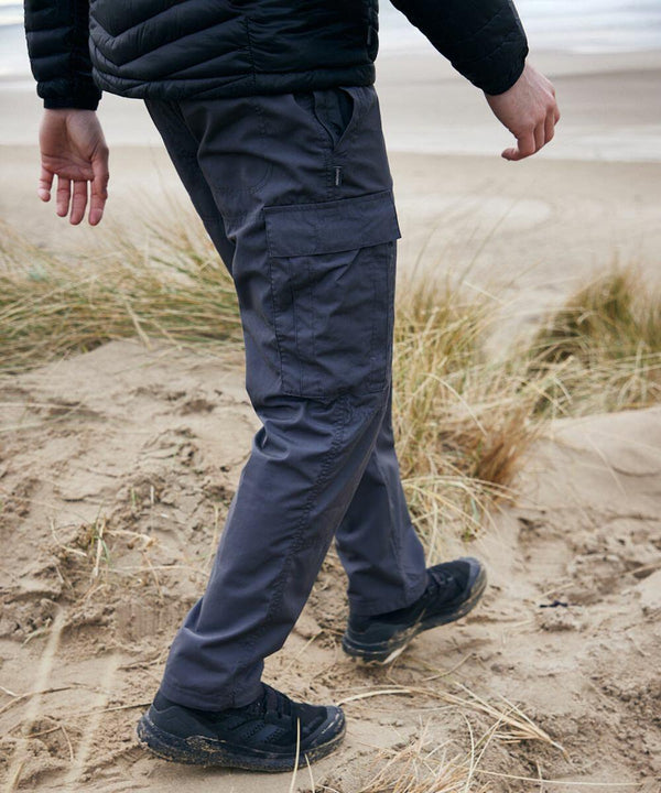 A person wearing Craghoppers CR231 cargo pants and black shoes walks through a sandy landscape with dry grasses.