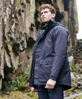 A man stands outdoors wearing a CR301 jacket by Craghoppers. He looks off into the distance; a rocky cliff is visible in the background.
