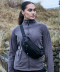 A person wearing a gray Craghoppers CR621 jacket and black crossbody bag stands outdoors with a stone wall and dry grasses in the background.