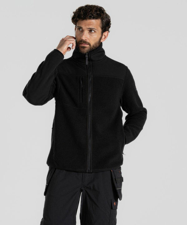 A man wearing a black Craghoppers CR703 fleece jacket and black cargo pants stands against a plain background, touching his ear with one hand.