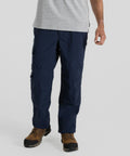 A person wearing navy blue CR706 cargo pants by Craghoppers, a light grey shirt, and brown hiking boots stands against a plain background.