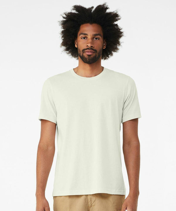 A man with an afro hairstyle wears a plain, light-colored Bella + Canvas CV001 T-shirt and beige pants. He stands against a plain white background, looking directly at the camera.