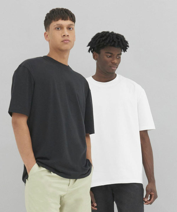 Two men are standing against a plain background, one in an EA006 by AWDis Ecologie black t-shirt and light pants, the other in an EA006 by AWDis Ecologie white t-shirt and dark pants.