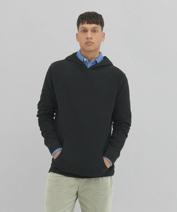 A person stands against a plain background, wearing an AWDis Ecologie EA041 black hoodie layered over a blue collared shirt, with hands in the hoodie pockets.