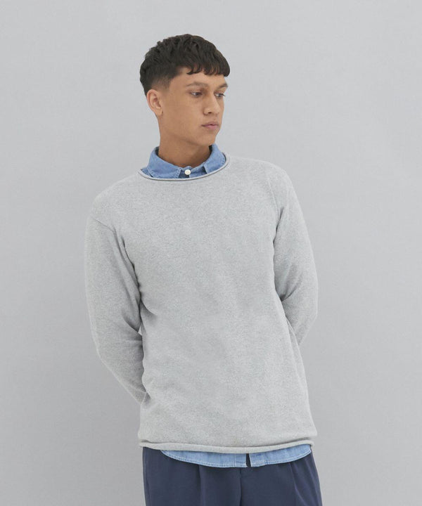 A person stands against a plain background, wearing an AWDis Ecologie EA060 over a blue collared shirt. They have short, dark hair and are looking slightly to the side.
