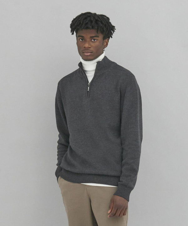 A man is standing against a plain background, wearing an EA061 by AWDis Ecologie over a white turtleneck and beige pants.