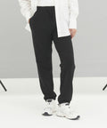 Person wearing an AWDis Ecologie EA070 white shirt, black pants, and white sneakers standing against a plain background.
