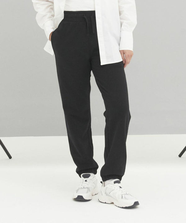 Person wearing an AWDis Ecologie EA070 white shirt, black pants, and white sneakers standing against a plain background.