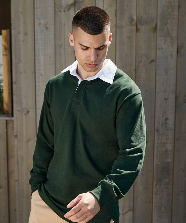 A person with short hair wearing a dark green long-sleeve shirt, identified as the FR01M by Front Row, with a white collar stands in front of a wooden fence, looking downwards.