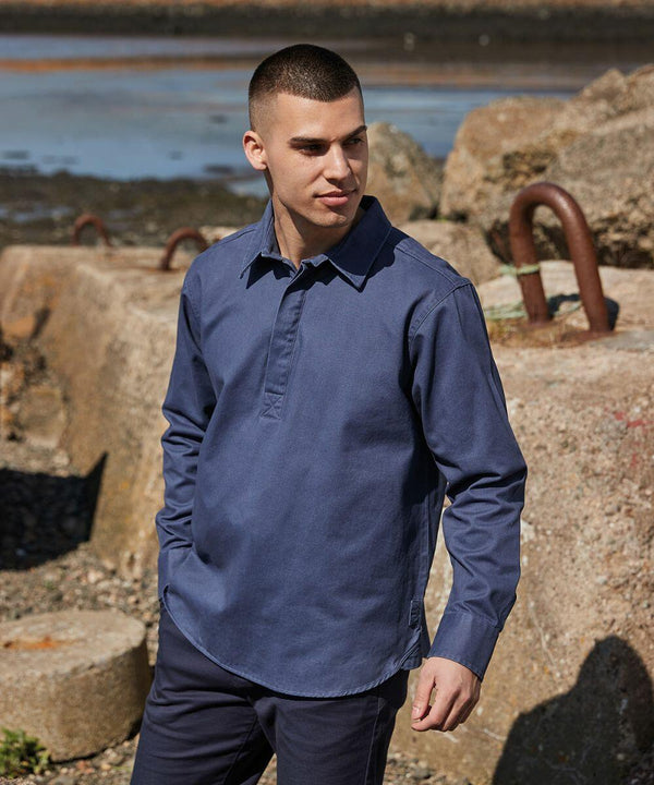 A man in a Front Row FR050 navy blue button-up shirt stands on a rocky seaside with large hooks embedded in the background rocks. He has short hair and is looking slightly to his right.