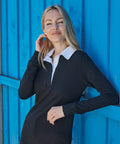 A person with long blonde hair poses in front of a bright blue wooden wall, wearing a black long-sleeve shirt with a white collar from Front Row called FR101.