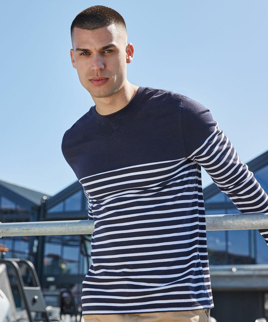 A man wearing a navy blue and white striped long-sleeve Front Row FR134 shirt leans against a metal railing with a blue sky and modern buildings in the background.