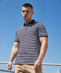 A man with a short haircut wears a navy and white striped Front Row FR230 polo shirt and beige pants, standing outdoors under a clear blue sky.