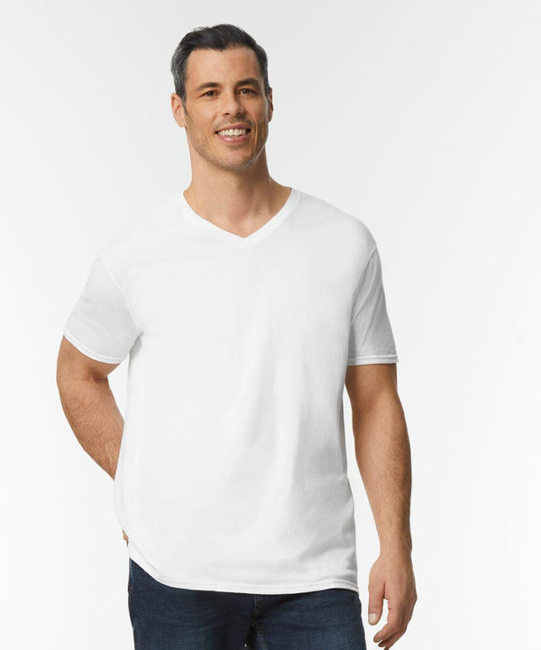 A person stands smiling, wearing a plain white Gildan GD010 V-neck T-shirt and dark jeans. The background is white.