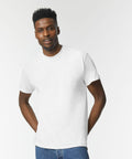 A man in a Gildan GD020 white t-shirt and blue jeans standing against a plain white background, looking at the camera with a slight smile, hands resting on his hips.