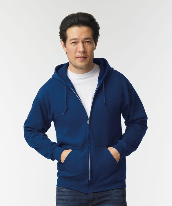 A person stands with hands in the pockets of a blue Gildan GD058 zip-up hoodie, over a white t-shirt, against a plain white background.