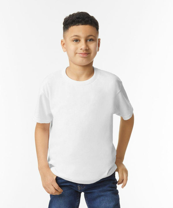 A young boy with short curly hair stands against a white background, wearing a plain white GD05B t-shirt by Gildan and blue jeans, with his right hand in his pocket.