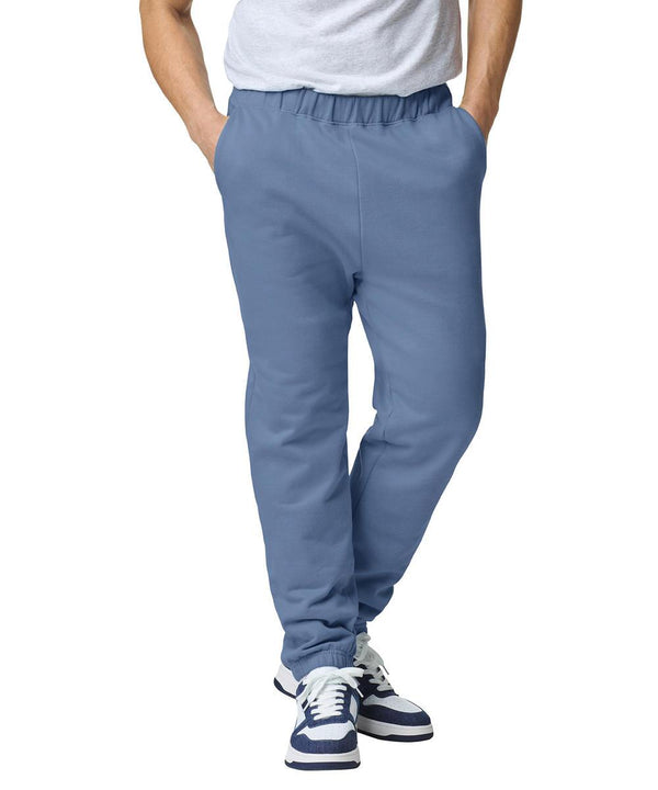 A person models Gildan Softstyle midweight adult pocket joggers in light blue, paired with a white t-shirt and blue-and-white trainers. Standing with hands in pockets, the head is not visible against the plain white background.