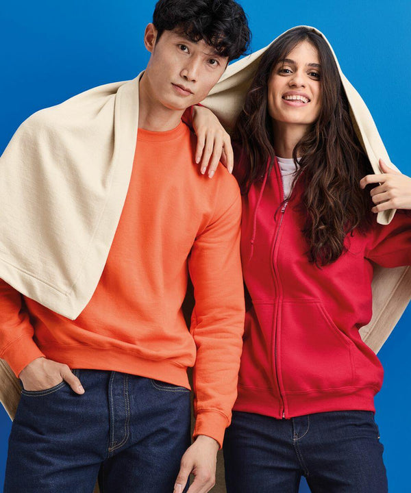 A man in an orange sweatshirt and a woman in a red hoodie, both with dark hair, stand against a blue background. A cream-colored GD101 from Gildan is draped over their heads.