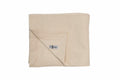 A folded GD101 blanket in beige, featuring a visible cloth label stitched on one corner, from the Gildan brand.