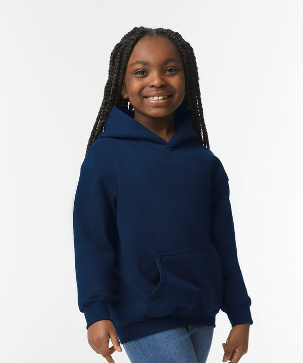 A smiling young girl with braided hair wearing a navy blue hoodie and jeans stands against a plain white background, showcasing the GD57B by Gildan.
