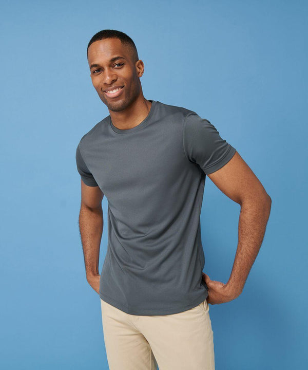 A person stands against a blue background, smiling and wearing a grey Henbury HB024 t-shirt and beige pants.