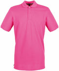 The Henbury HB101 is a vibrant pink polo shirt featuring short sleeves and a collar, complete with buttons at the neck. It is showcased against a clean white background.