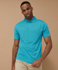 A man wearing a bright blue HB475 polo shirt from Henbury and beige pants poses against a plain brown background.