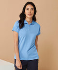 Person standing against a plain background, wearing a light blue Henbury HB476 short-sleeved polo shirt and dark pants.