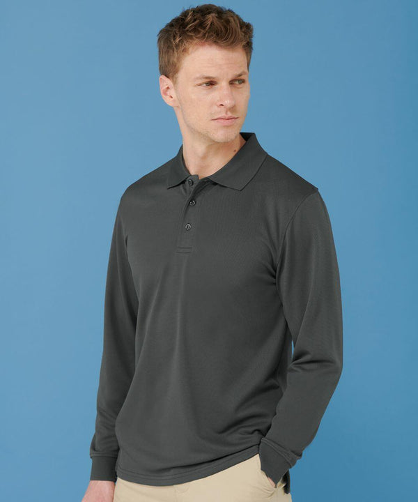 A man wearing a long-sleeved, charcoal-colored Henbury HB478 polo shirt and beige pants stands against a solid blue background. He is looking to the side with a neutral expression.