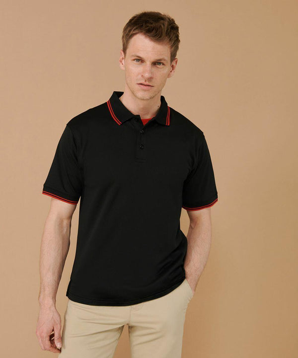 A man with short hair wearing a black Henbury HB482 polo shirt with red trim and beige pants stands against a beige background.
