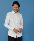 A person wearing a white Henbury HB511 button-up shirt smiles while looking down, standing in front of a blue background.