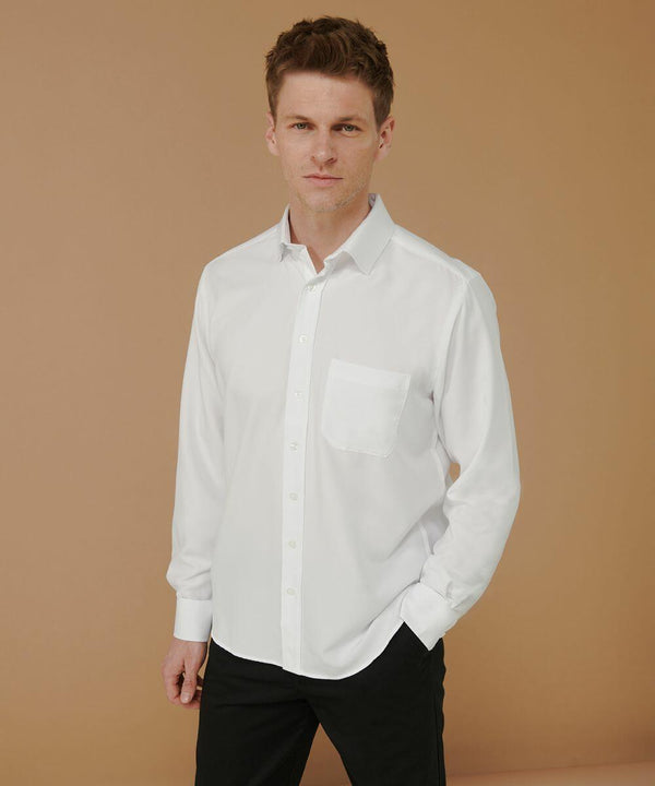 A person standing against a light brown background, wearing a white Henbury HB590 long-sleeve button-up shirt and black pants.