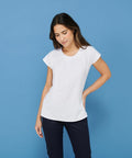 A woman in a white short-sleeved Henbury HB597 blouse and navy pants stands against a blue background, looking down with a slight smile.