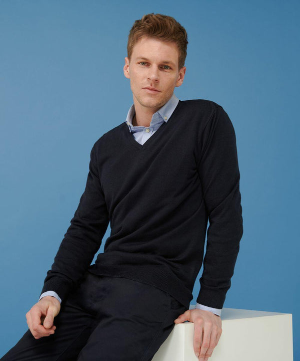 A person with short hair wearing a dark long-sleeve Henbury HB720 sweater over a light blue collared shirt sits on a white block against a blue background.