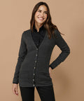 Person wearing a dark gray Henbury HB723 button-up cardigan over a black collared shirt, standing against a plain beige background with hands in pockets and smiling.